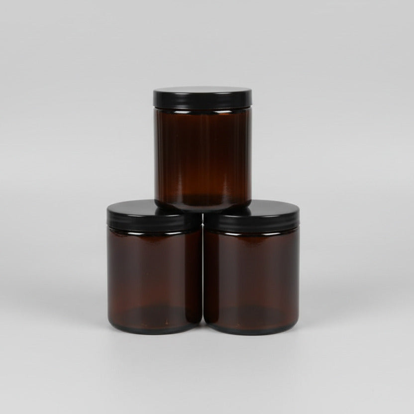 Three amber glass jars with black lids on a light gray background
