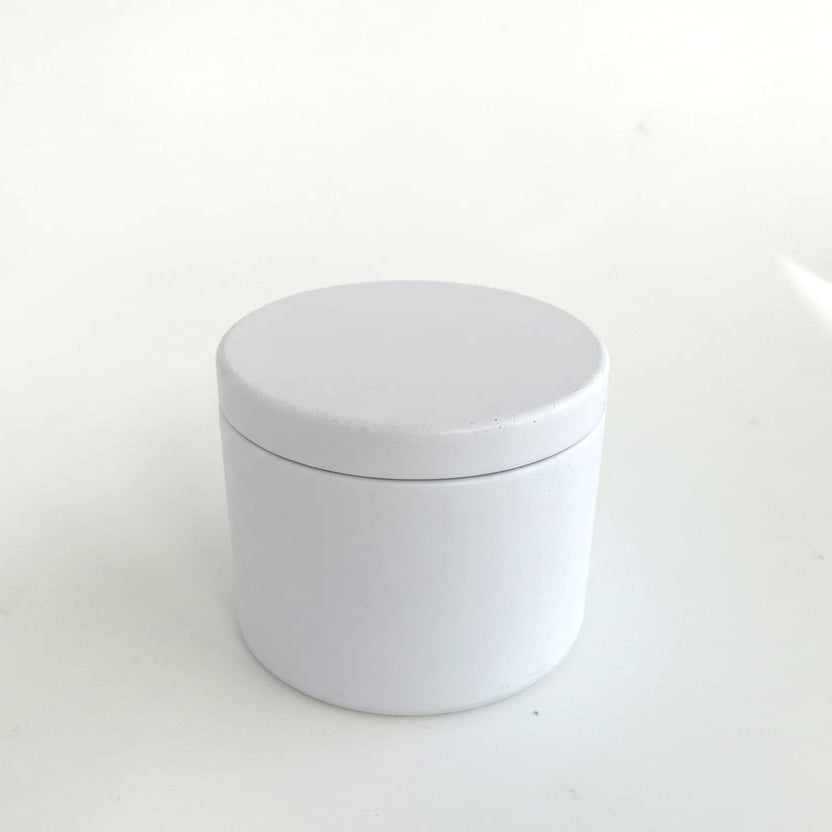 White candle tin container with a lid on a light gray background